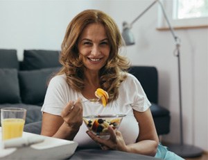 Woman with dental bridge in Plano eating fruit salad