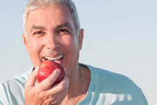 Man with implant dentures biting an apple.