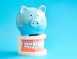 Piggy bank atop model teeth representing the cost of dental emergencies in Plano