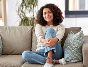 A young woman sitting on a couch and smiling after SureSmile Treatment