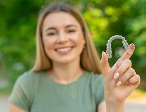 Patient smiling while holding up clear aligner