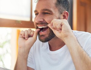 Man smiling while flossing his teeth in bathroom
