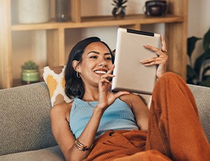 Smiling woman looking at tablet while relaxing on couch