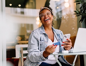 Woman laughing and sitting at laptop with phone