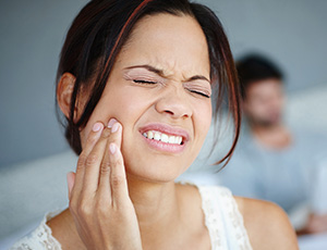 Grimacing woman in need of emergency dentistry holding cheek