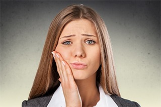 A young woman holding her cheek in pain before root canal therapy