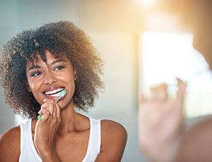 Smiling woman in white tank top brushing her teeth