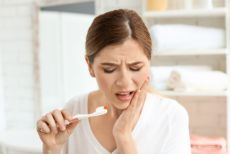 Woman brushing her teeth with a painful expression
