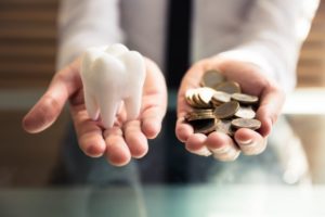 Model tooth in outstretched hand, pile of coins in another