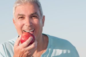 Man with dentures in Plano biting an apple. 