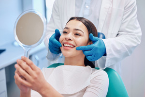 Woman checking smile in mirror after dental appointment
