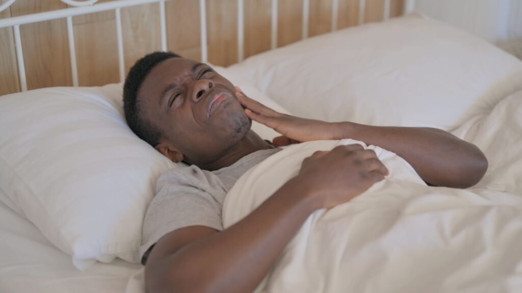Person in bed pressing hand to jaw in pain